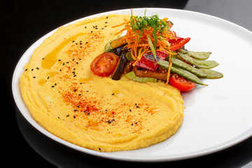 Hummus with baked vegetables.  On a black  background. Vegetarian dish.