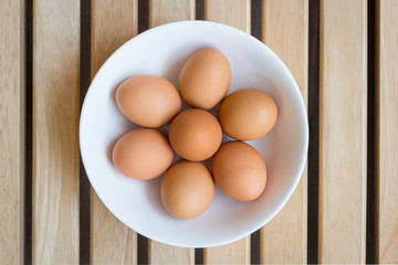 Eggs with brown shells in ceramic bowl on a brown wooden table