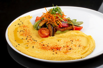 Hummus with baked vegetables.  On a black  background. Vegetarian dish.