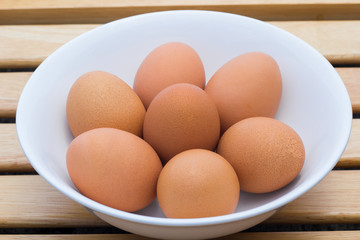 Eggs with brown shells in ceramic bowl on a brown wooden table