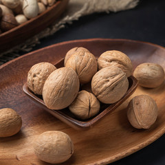 nuts on a square wooden bowl and an oval wooden tray on a dark background and burlap