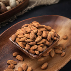 nuts on a square wooden bowl and an oval wooden tray on a dark background and burlap