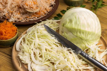 Sliced raw cabbage, knife on cutting board. Carrots and salted cabbage in plate. Homemade...