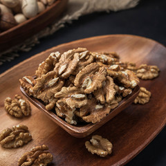 nuts on a square wooden bowl and an oval wooden tray on a dark background and burlap