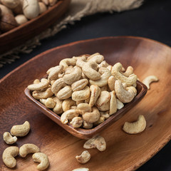 nuts on a square wooden bowl and an oval wooden tray on a dark background and burlap