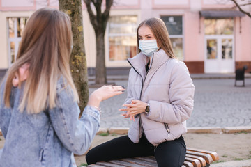 Girls in masks. Coronavirus theme. Women sitting on the bench in the city center during quarantine