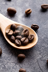 Roasted coffee beans in wood spoon with steam on black background.