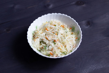 Fresh cabbage salad with carrot and dill in white bowl on black wooden background