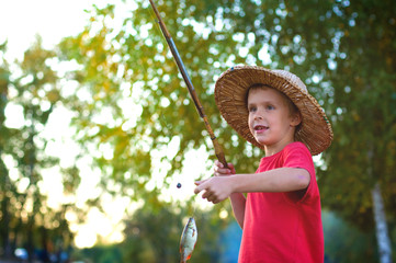 horizontal portrait of a happy boy with fishing rod and fish on a background of green foliage