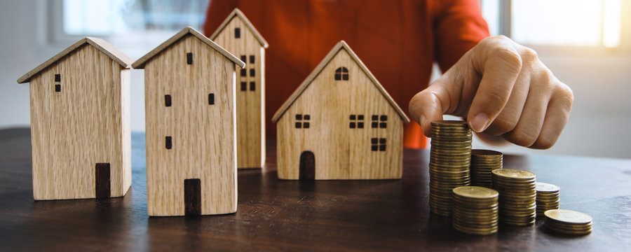 Save to real estate, property owner get money to home concept, small wooden house model on table with hand stacked coins to rent or buy above mentioned residence with cash to bank agency