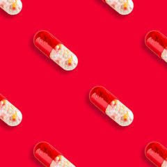 Medical seamless pattern made with capsule pills on red background.