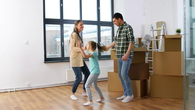 mortgage, family and real estate concept - happy mother, father and little daughter with stuff in boxes moving to new home and dancing