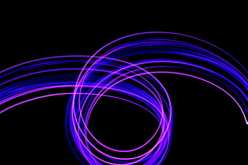 Long exposure photograph of neon purple streaks of light in an abstract swirl, parallel lines pattern against a black background. Light painting photography.