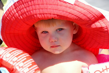 portrait of a little girl in the shadow of a large bright red hat