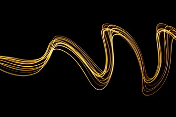 Long exposure photograph of neon gold streaks of light in an abstract swirl, parallel lines pattern against a black background. Light painting photography.