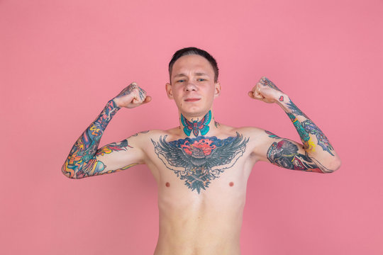 Strong gesture. Portrait of young man with freaky appearance on pink background. Unusual look with huge tattooes. Doing daily routine. Human emotions, facial expression, ad concept. Youth culture.