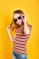 Little girl wearing sunglasses smiling and posing on yellow background