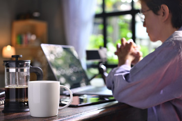 A coffee press and a cup on a work desk with a person working from home