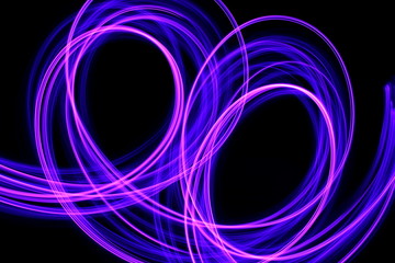 Long exposure photograph of neon purple streaks of light in an abstract swirl, parallel lines pattern against a black background. Light painting photography.