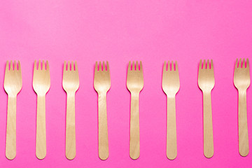 eco-friendly disposable wooden forks on a pink background. isolate