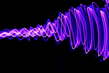 Long exposure photograph of neon purple streaks of light in an abstract swirl, parallel lines pattern against a black background. Light painting photography.