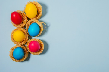 Painted Easter eggs lie in pasta nests on a blue background. Soft focus, horizontal background, flat lay.