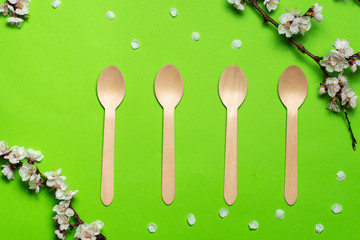 Four disposable spoons made of natural materials, wooden utensils. Green background with floral...