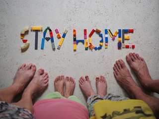 The concept of self-isolation during quarantine from coronavirus. Toy blocks are laid out to encourage you to stay at home, and next to the feet of all family members: mom, dad, son and daughter