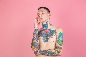 Thinking. Portrait of young man with freaky appearance on pink background. Unusual look with huge tattooes. Doing daily routine. Human emotions, facial expression, sales, ad concept. Youth culture.
