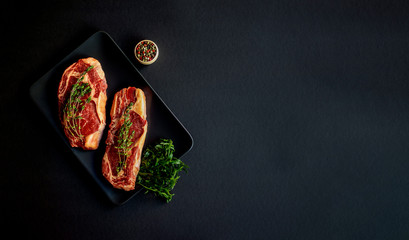 Two raw Rib eye japanese steaks with spices on a black background