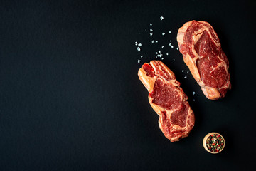 Two raw Rib eye Japanese steaks with spices on a black background