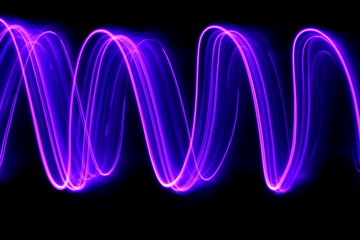 Long exposure photograph of neon purple streaks of light in an abstract swirl, parallel lines pattern against a black background. Light painting photography.