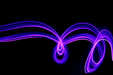 Long exposure photograph of neon purple streaks of light in an abstract swirl, parallel lines pattern against a black background. Light painting photography.