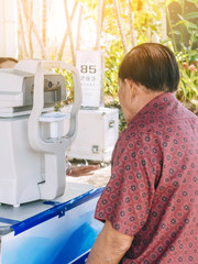 Elderly man checking eye vision on optometry equipment with a mobile hospital unit for eye examination services for the general public at public park.