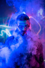 Head of young man in eyeglasses standing in smoke and blue neon light