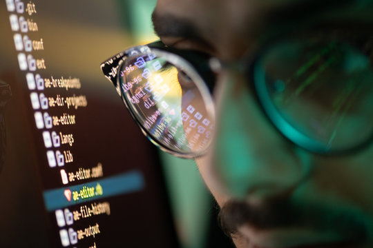 Part of face of young programmer in eyeglasses with reflection of decoded data