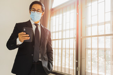 Businessman wearing protective mask preventing covid - 19 using cell phone.