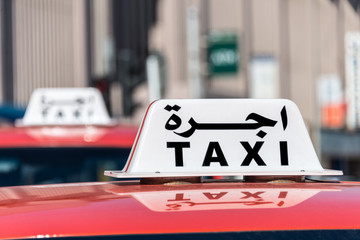 A sign on top of a red car says taxi in English and Arabic.