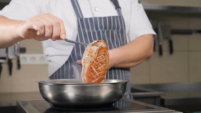 Unrecognizable male chef flipping piece of duck meat frying in hot pan with olive oil. Slow motion footage. Cooking classic Confit Duck in French restaurant, close-up. Shot in hd.