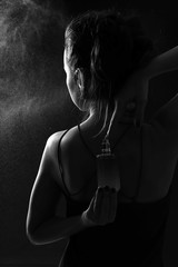 Silhouette of beautiful young woman with perfume on dark background
