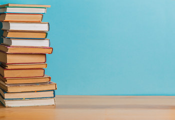 A simple composition of many hardback books, raw books on a wooden table and a bright blue background. Going back to school. Copy space. Education.