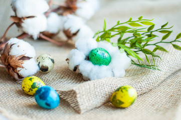 colorful Easter quail eggs on a linen bag on the background of a branch of cotton and with a green twig and leaves