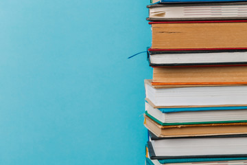 A simple composition of many hardback books, raw books on a wooden table and a bright blue background. Going back to school. Copy space. Education.