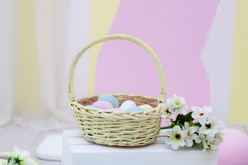 Fototapeta na wymiar Basket of colorful easter eggs with flowers. Wicker yellow basket with Easter eggs on color background. View with copy space. basket with easter eggs and daisies on a wooden table. Spring decor. Farm