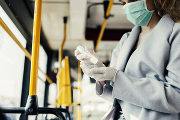 Woman wearing surgical protective mask disinfecting hands a public transportation