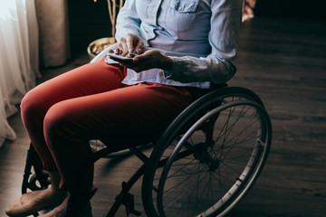 Obraz premium close up of a young woman in a wheelchair with a mobile phone in her hands at home. Recovery and healthcare concepts.