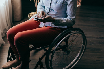 Fototapeta na wymiar close up of a young woman in a wheelchair with a mobile phone in her hands at home. Recovery and healthcare concepts.