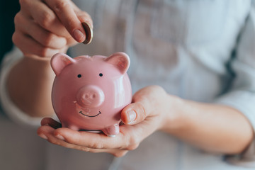 female hands hold a pink piggy bank and puts a coin there. The concept of saving money or savings,...