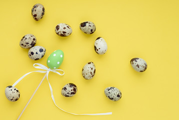 A chaotic pattern of Easter eggs on a yellow background. Happy easter banner. One decorative egg on a stick among small quail eggs