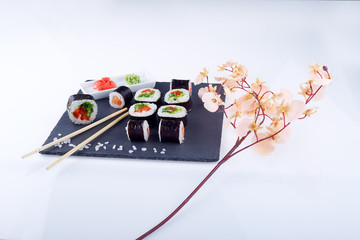 Sushi set with ginger and wassabi on a black square plate of stone on a light background. Near a sprig of sakura.